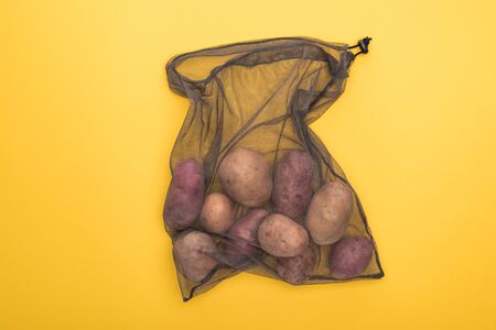 top view of potatoes in eco friendly black mesh bag isolated on yellow