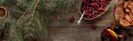 top view of red spiced mulled wine with berries, anise, orange slices and cinnamon on wooden rustic table near fir branch, panoramic shotの写真素材