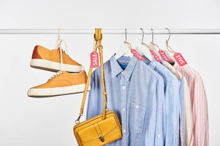 sneakers, bag and elegant shirts hanging with sale labels isolated on white