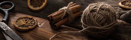 close up view of cinnamon sticks, scissors, ball of thread on wooden background with dried citrus slices, panoramic shotの写真素材