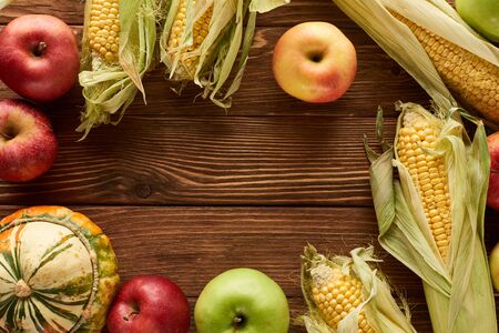 top view of uncooked sweet corn, ripe apples and pumpkin on wooden surface with copy spaceの写真素材