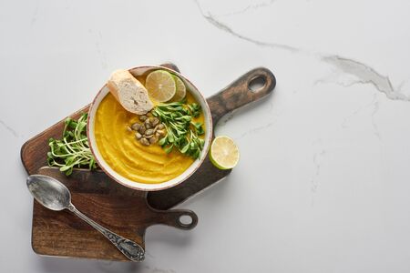 top view of autumnal mashed pumpkin soup on wooden cutting board on marble surface with silver spoonの写真素材