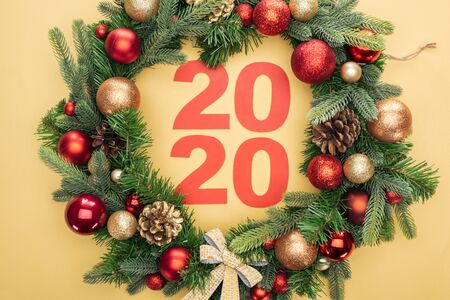 top view of paper 2020 numbers in christmas wreath with baubles on yellow backgroundの写真素材