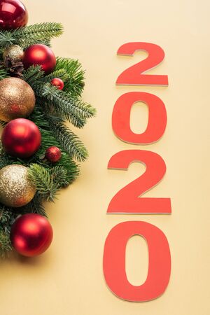 red 2020 numbers near christmas tree branch with baubles on yellow background