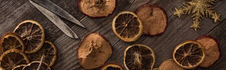 top view of dried citrus and apple slices near snowflake, rope and scissors on wooden surface, panoramic shotの写真素材