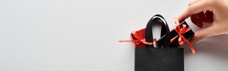 cropped view of woman putting small gift boxes in black shopping bag on white background, panoramic shotの写真素材