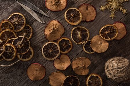 top view of dried citrus and apple slices near snowflake, rope and scissors on wooden surfaceの写真素材