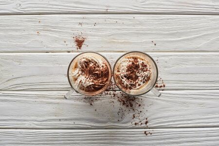 top view of cacao with whipped cream and cacao powder in mugs on white wooden tableの写真素材