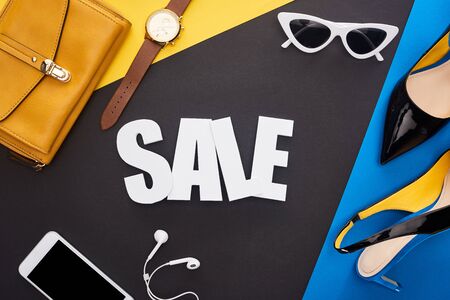 top view of sale lettering near accessories and smartphone with earphones on blue, yellow and black backgroundの写真素材