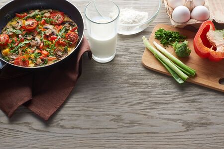 delicious homemade omelet in frying pan with ingredients on table