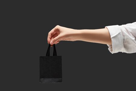 cropped view of woman holding small black shopping bag in hand isolated on blackの写真素材