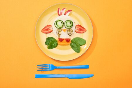 top view of plate with fancy cow made of food for childrens breakfast near cutlery on orange backgroundの写真素材
