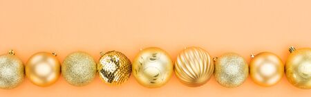 top view of golden christmas baubles in row on orange background, panoramic shot