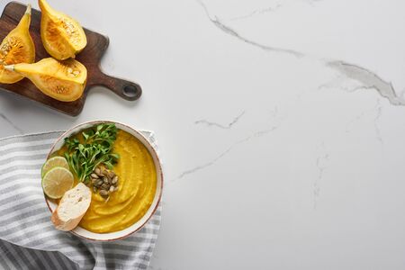 top view of tasty mashed pumpkin soup on wooden cutting board with ingredients on marble surfaceの写真素材