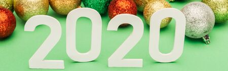 white 2020 numbers near multicolored Christmas baubles on green background, panoramic shotの写真素材
