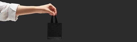 cropped view of woman holding small black shopping bag in hand isolated on black, panoramic shotの写真素材