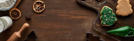 top view of glazed Christmas cookies near ingredients on wooden table, panoramic shot