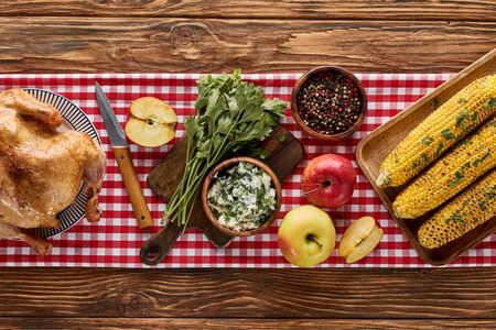 top view of roasted turkey, grilled corn and apples with parsley and peppercorn served on wooden table with red napkinの写真素材