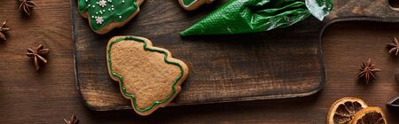 top view of Christmas tree cookies, pastry bag and winter spices on wooden table, panoramic shot