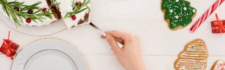 cropped view of girl with christmas cake and cookies on white wooden table