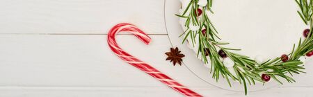 top view of christmas pie with icing and rosemary on white wooden table with candy cane