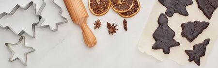 top view of raw dough for chocolate Christmas cookies with rolling pin on white background near...