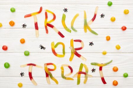 top view of trick or treat lettering made of colorful gummy sweets on white wooden table with spiders and bonbons, Halloween treatの写真素材