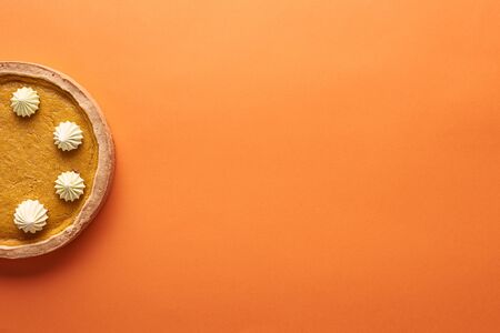top view of delicious pumpkin pie with whipped cream on orange surface with copy spaceの写真素材