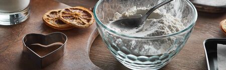 heart shaped dough mold, flour with spoon in glass bowl, dried citrus slices on wooden table,...