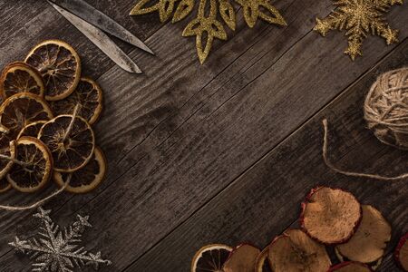 top view of dried citrus and apple slices near snowflakes, rope and scissors on wooden surface with copy spaceの写真素材