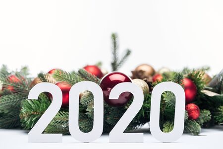 paper 2020 numbers near Christmas tree wreath with baubles isolated on white