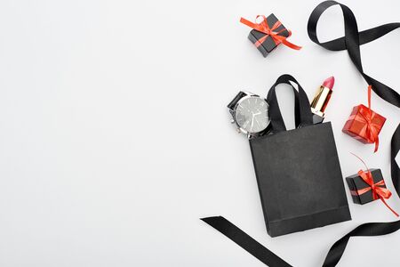 top view of small shopping bag with male wristwatch and female lipstick near ribbon and presents on white backgroundの写真素材