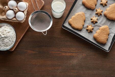 top view of Christmas cookies on oven tray near ingredients on wooden table