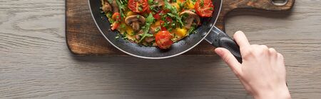 top view of woman cooking omelet with mushrooms, tomatoes and greens on frying panの写真素材
