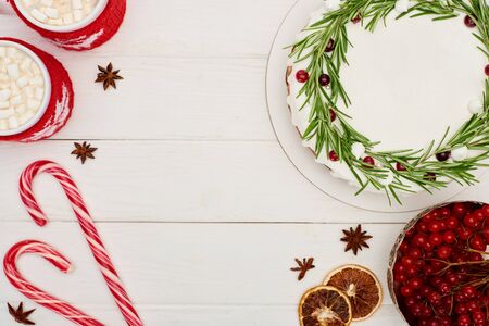 top view of christmas pie, viburnum berries, candy canes and two cups of cocoa with marshmallows on white wooden tableの写真素材