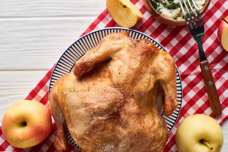 top view of roasted turkey, apples served on white wooden table with red plaid napkinの写真素材