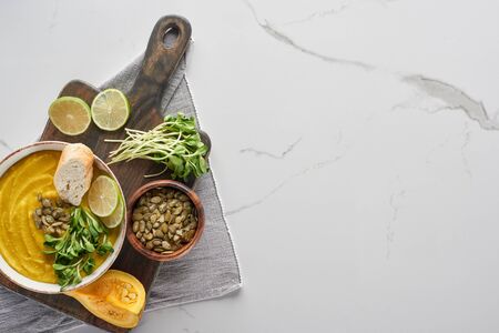 top view of delicious mashed pumpkin soup on wooden cutting board on marble surface with ingredientsの写真素材