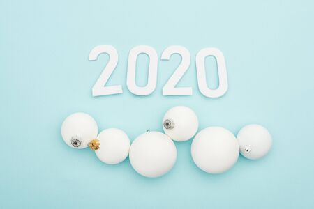 top view of white 2020 numbers near Christmas baubles on light blue background