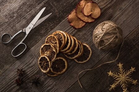 top view of thread, scissors and dried citrus and apple slices on wooden background with snowflake