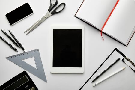 top view of clipboard, notebook, pens, pencils, scissors, triangle ruler, calculator, smartphone and...