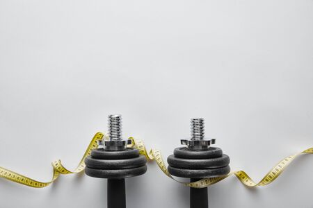 top view of heavy black dumbbells near measuring tape on whiteの写真素材