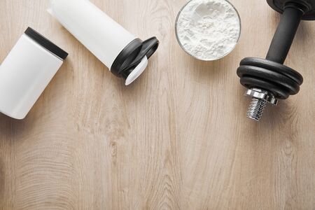 top view of dumbbell near sports bottle and jar on wooden surfaceの写真素材