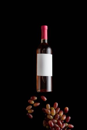 top view of bottle with rose wine and blank white label near grape isolated on blackの写真素材