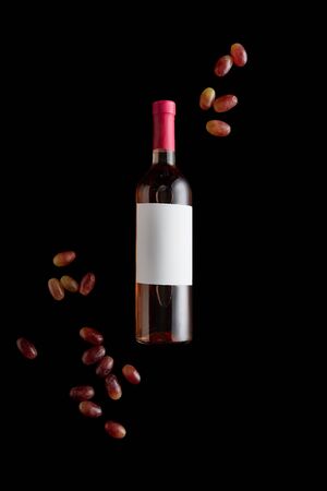 top view of rose wine bottle with blank white label near ripe grape isolated on blackの写真素材