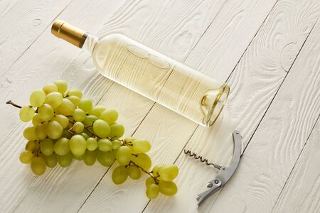 bottle with white wine near grape and corkscrew on white wooden surfaceの写真素材