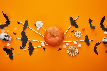 top view of pumpkin, skulls, bats and spiders with confetti on orange background, Halloween decorationの写真素材