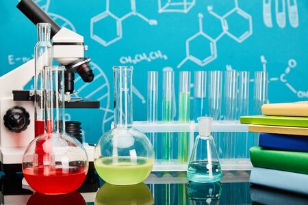 books, microscope, glass test tubes and flasks with colorful liquid on blue background with molecular structureの写真素材