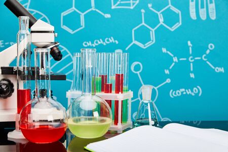 microscope, glass test tubes and flasks with colorful liquid near open copybook on blue background with molecular structureの写真素材