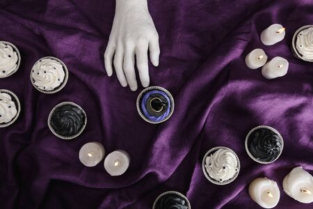 top view of decorative hand near tasty Halloween cupcake with blue cream and witch hat near burning...