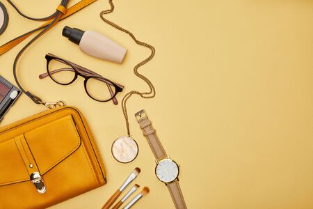 top view of bag near glasses, necklace and watch isolated on yellowの写真素材